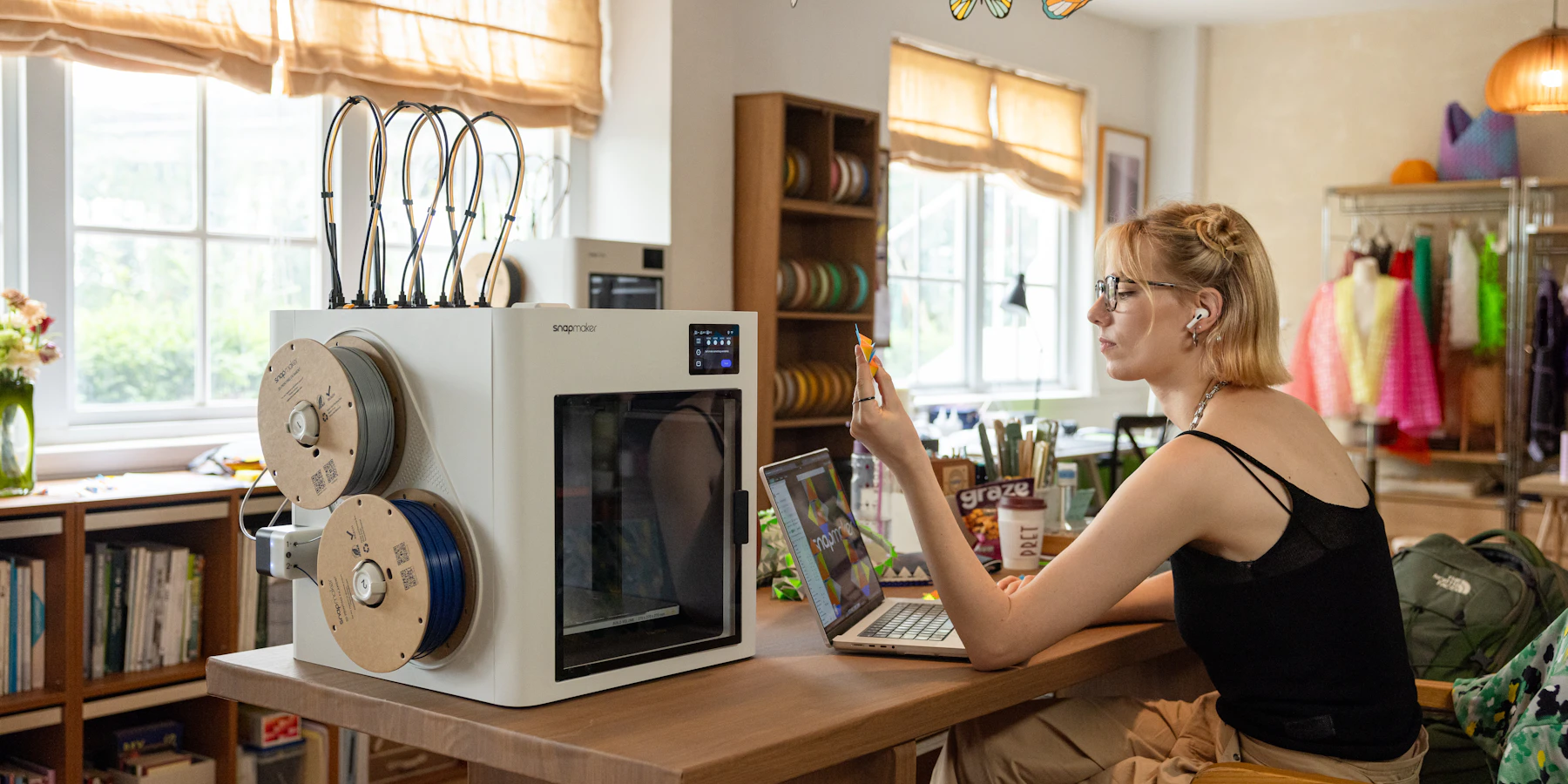 A designer examining a small 3D-printed prototype beside a printer and laptop.